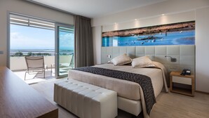 Ein modernes Schlafzimmer mit einem großen Bett, einer Bank, einem Nachttisch und Meerblick durch eine Schiebetür.