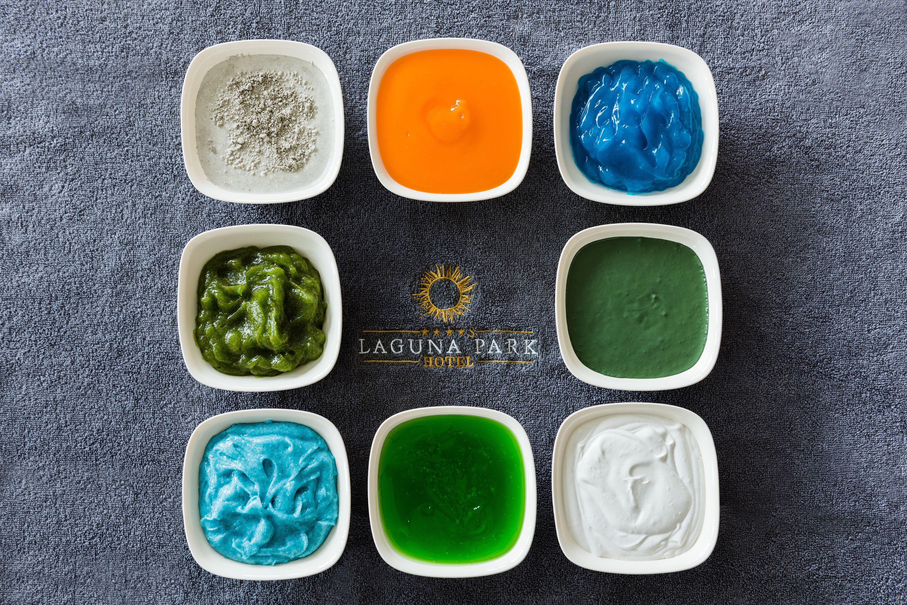 Eight bowls of colorful dips arranged on a table.
