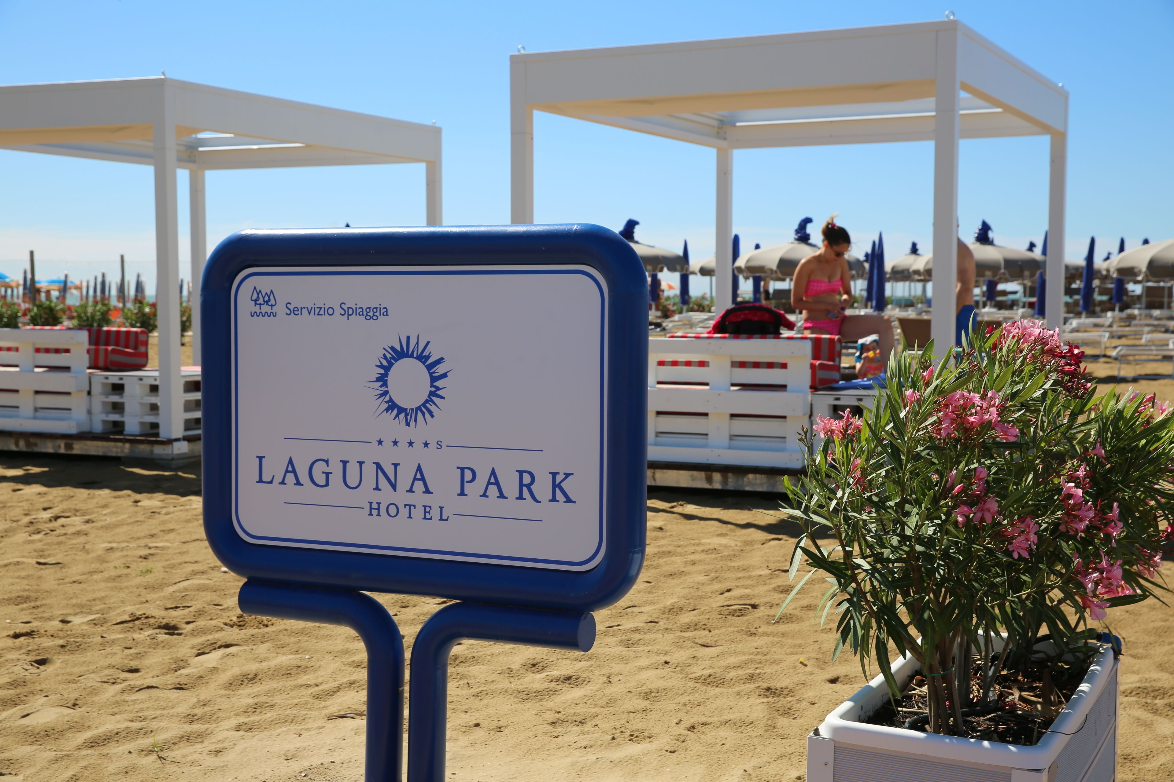 A sign for Laguna Park Hotel with a sun emblem, surrounded by beach umbrellas and a potted plant.