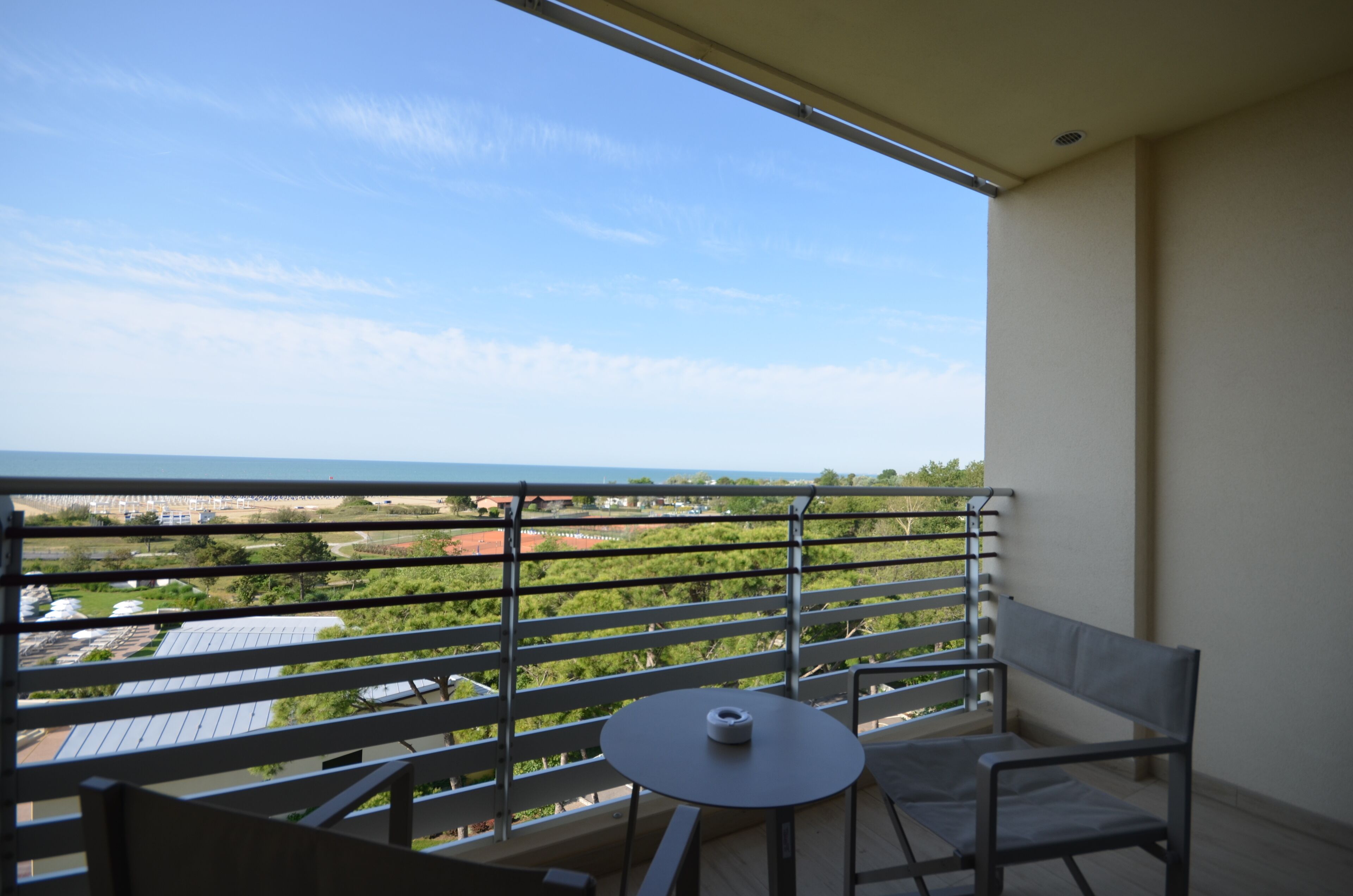 Un balcon avec une table et des chaises, offrant une vue sur la mer et la verdure.