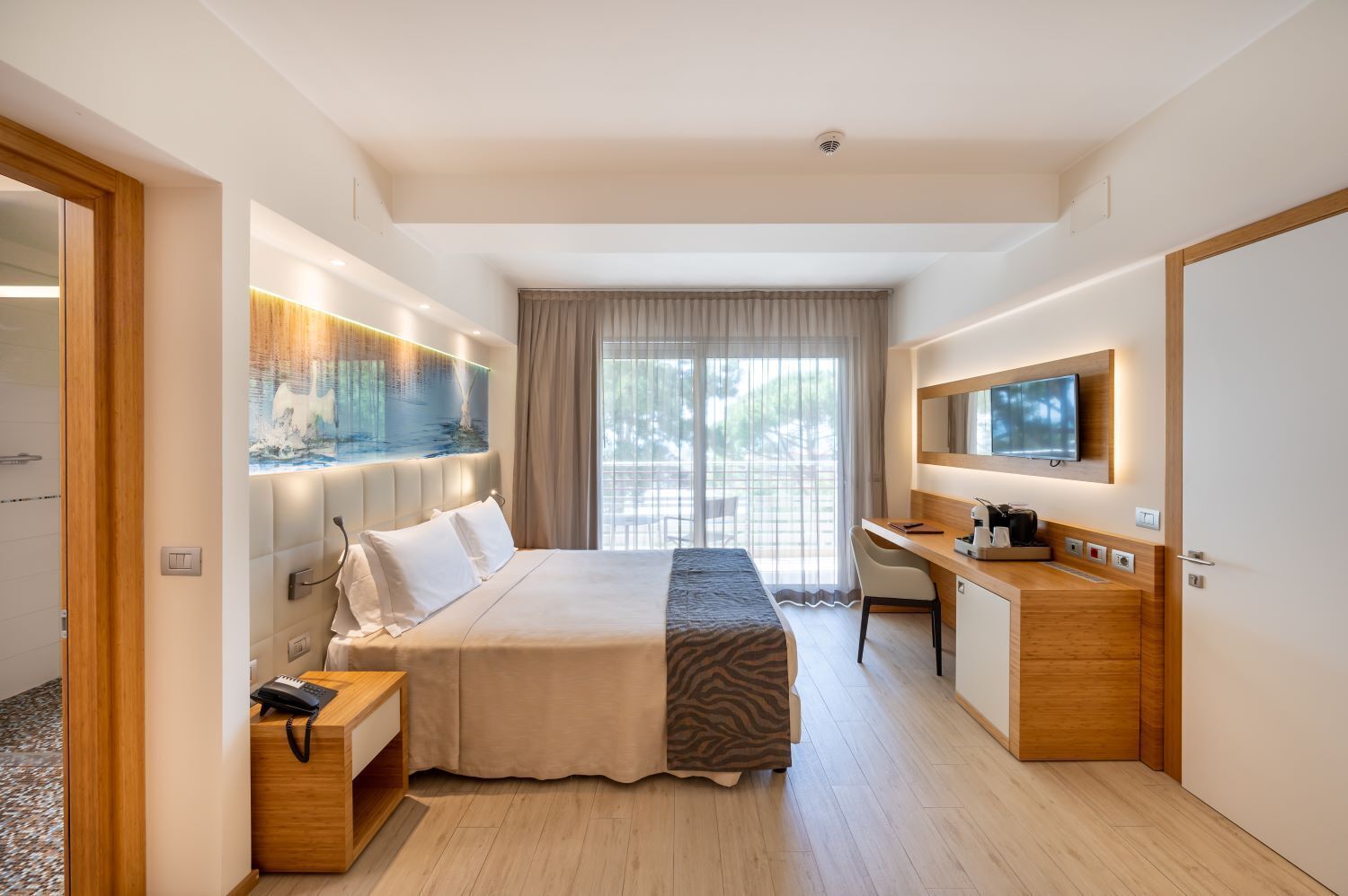 Ein modernes Hotelzimmer mit einem großen Bett, einem Schreibtisch, einem Fernseher und einem durch eine offene Tür einsehbaren Badezimmer.