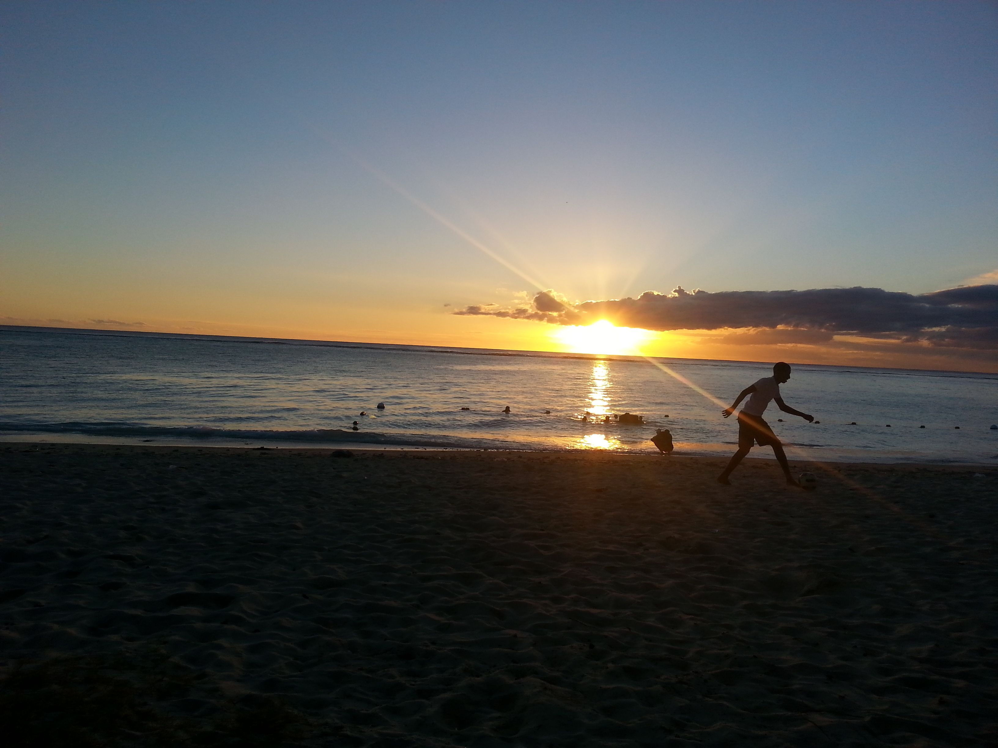 Eine Szene am Strand bei Sonnenuntergang, eine Person spielt mit einem Ball, und das Meer ist zu sehen.