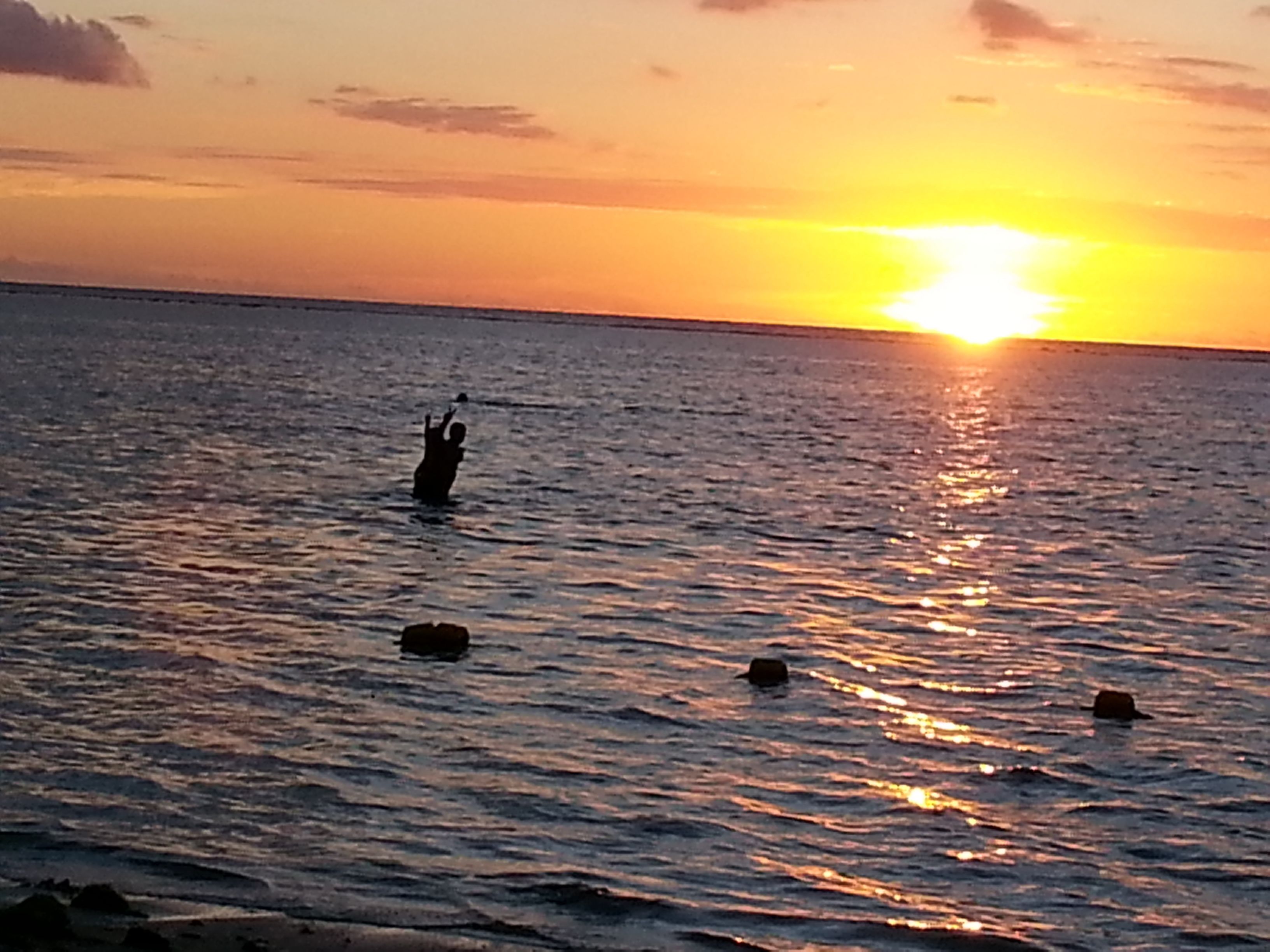 Un atardecer sobre un mar tranquilo, con una persona de pie en el agua.