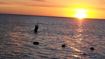 Un atardecer sobre un mar tranquilo, con una persona de pie en el agua.