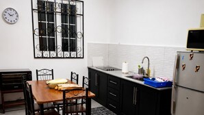 Una cocina con una mesa de comedor, sillas, un refrigerador, un lavamanos y un reloj en la pared.