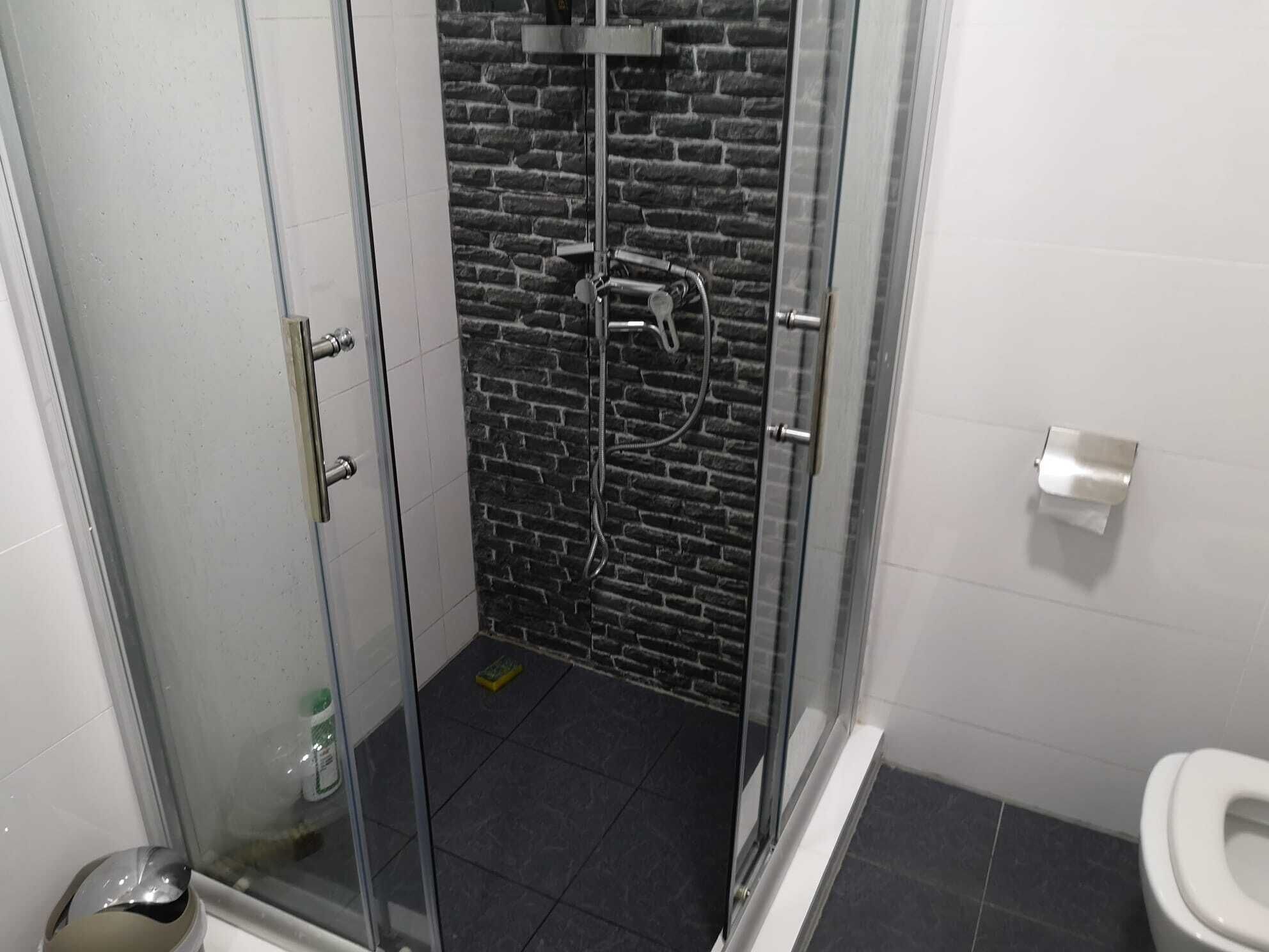 Un baño con ducha de mampara de vidrio, inodoro y cubo de basura.