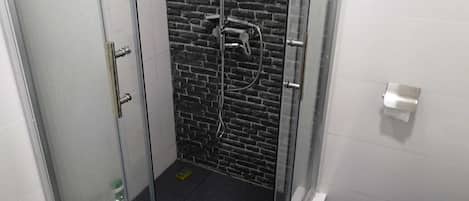 Un baño con ducha de mampara de vidrio, inodoro y cubo de basura.