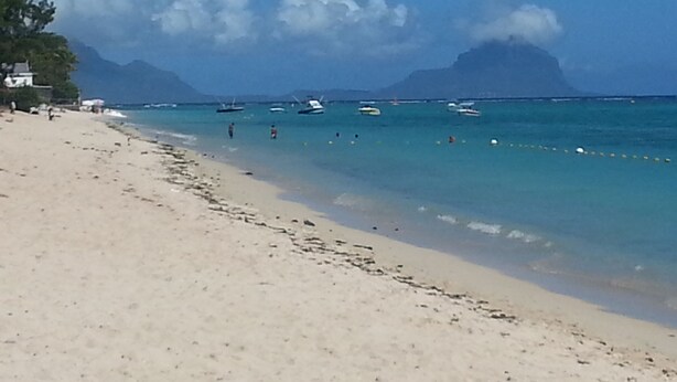 Una playa con agua turquesa cristalina, barcos y montañas al fondo.