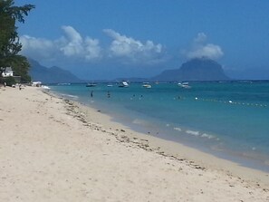 Una playa con agua turquesa cristalina, barcos y montañas al fondo.