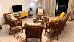 Una sala de estar con muebles de mimbre, un televisor de pantalla plana, una mesita con velas y un balcón con cortinas.