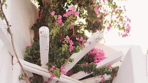 A person sitting in a narrow outdoor space with a blue door, white walls, and a wooden pergola with pink flowers. - La Stella Stay (Mykonos)