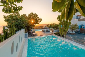 Una piscina con vistas al atardecer, rodeada de follaje y sillones de descanso.