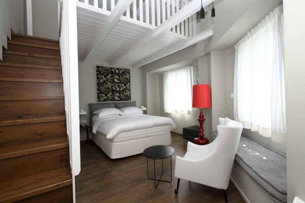 A bedroom with a bed, a chair, a small table, and a staircase.