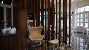 A modern interior with a reception desk, a lounge chair, and a seating area with tables and chairs. - Hotel Metropolis (Ioannina)