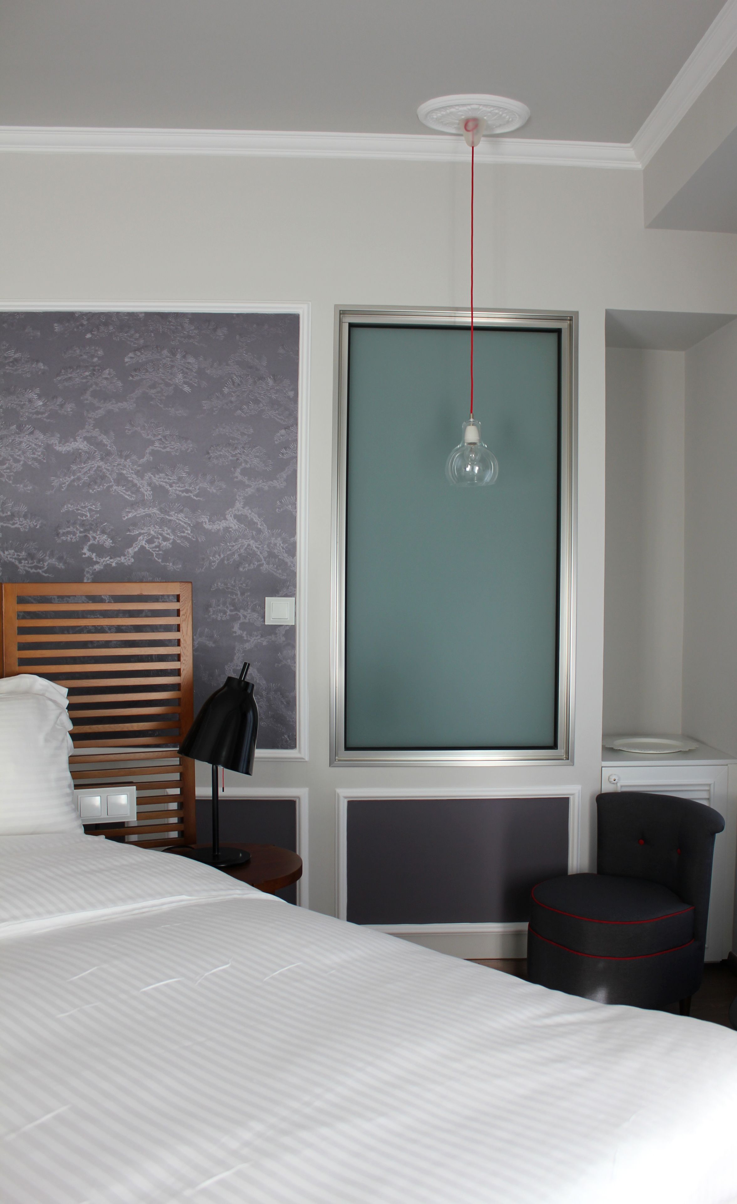 Habitación de hotel con cama, mesita de noche, lámpara, silla y ventana con vistas.