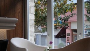 A room with two white chairs facing a window with a view of a building and trees. - Hotel Metropolis (Ioannina)