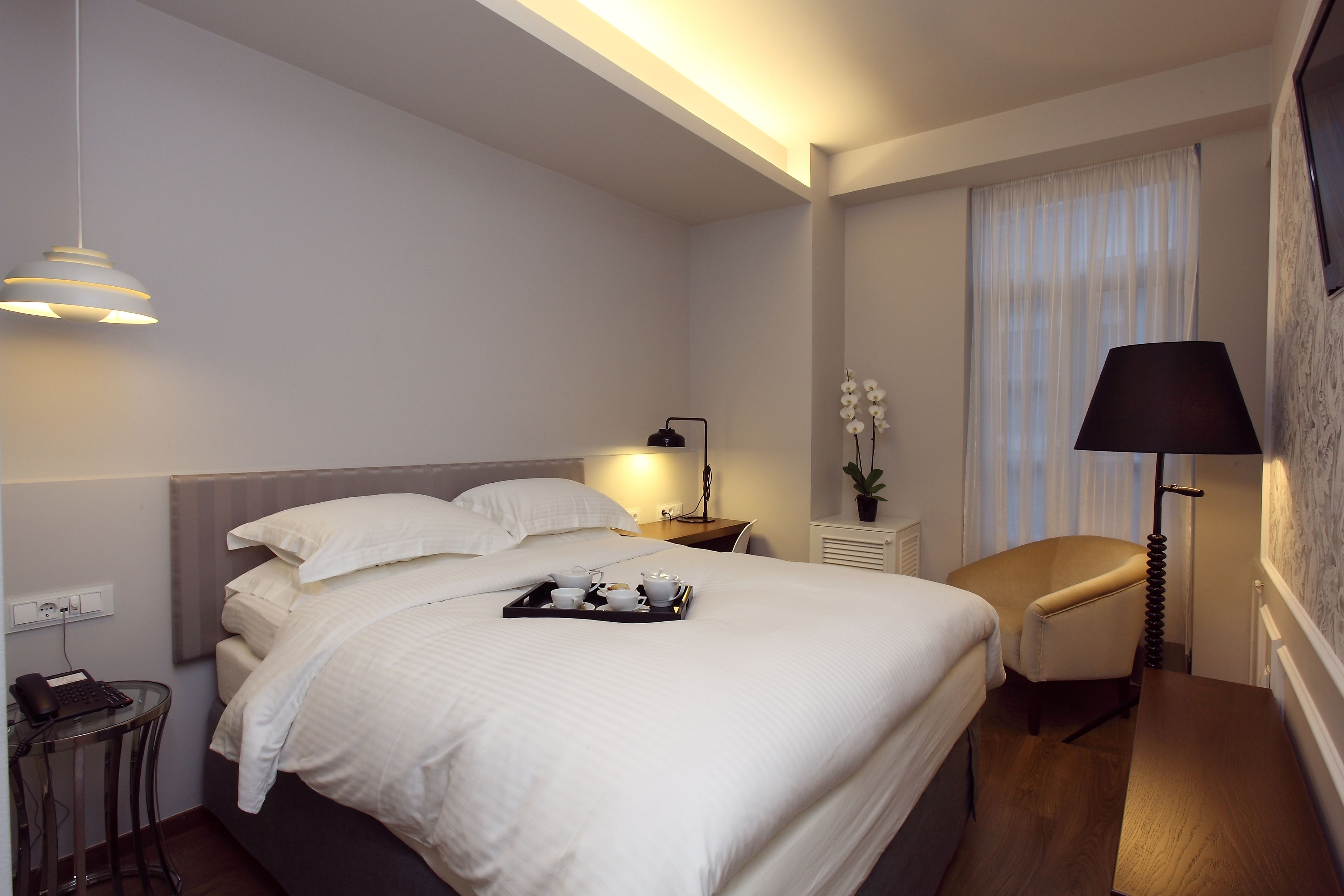 Habitación de hotel con una cama grande, mesita de noche, lámpara y una pequeña mesa con un teléfono y cargador.