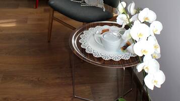 A room with a wooden floor, a red chair, a small round table with a white cup and saucer, a white orchid plant, and a red floor lamp.