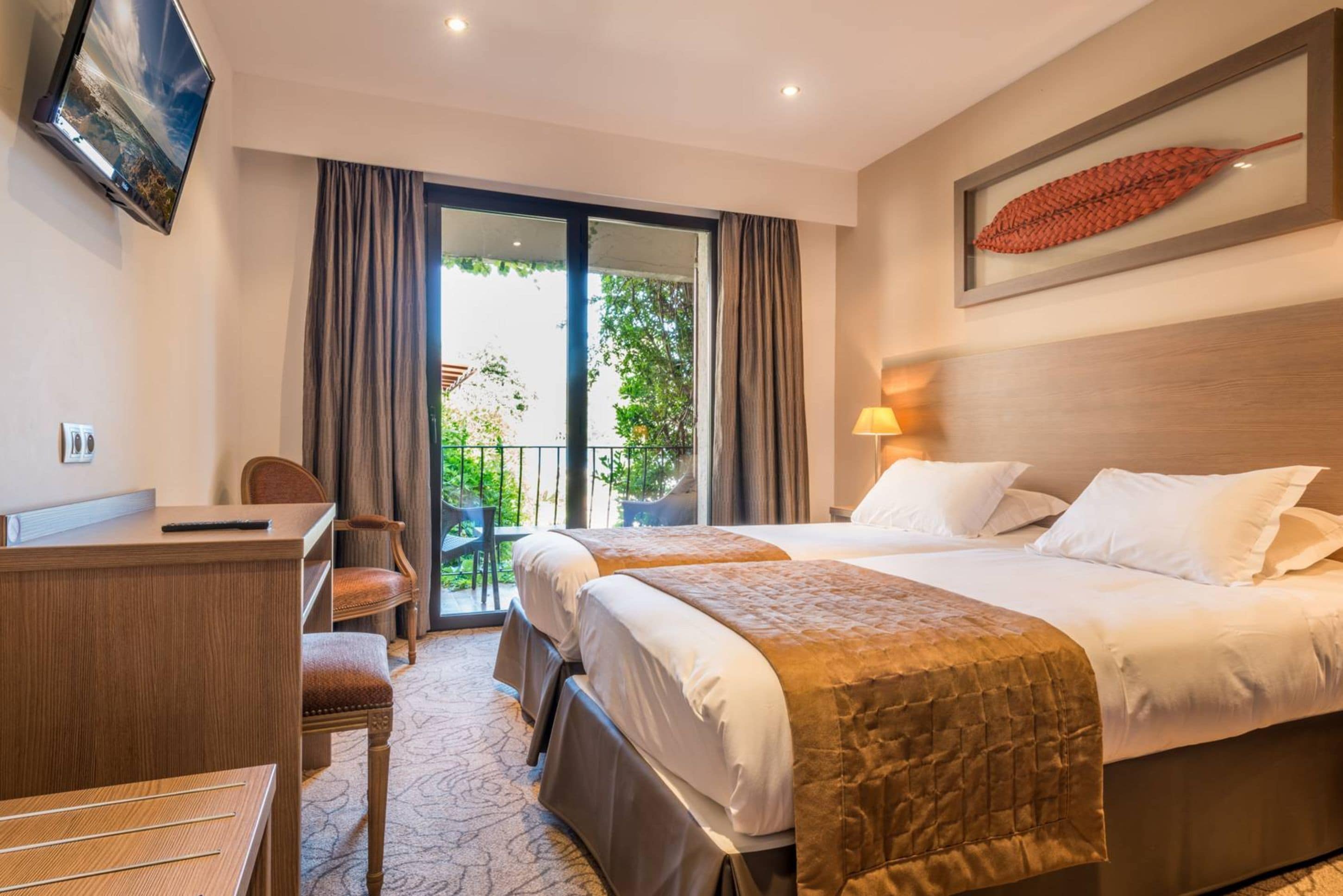 Une chambre d’hôtel avec deux lits, un bureau, une chaise, une télévision et un balcon avec des rideaux.