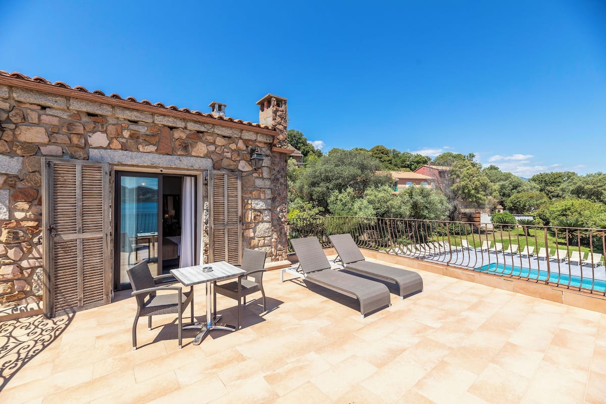 A stone building with a terrace, outdoor seating, and a pool.