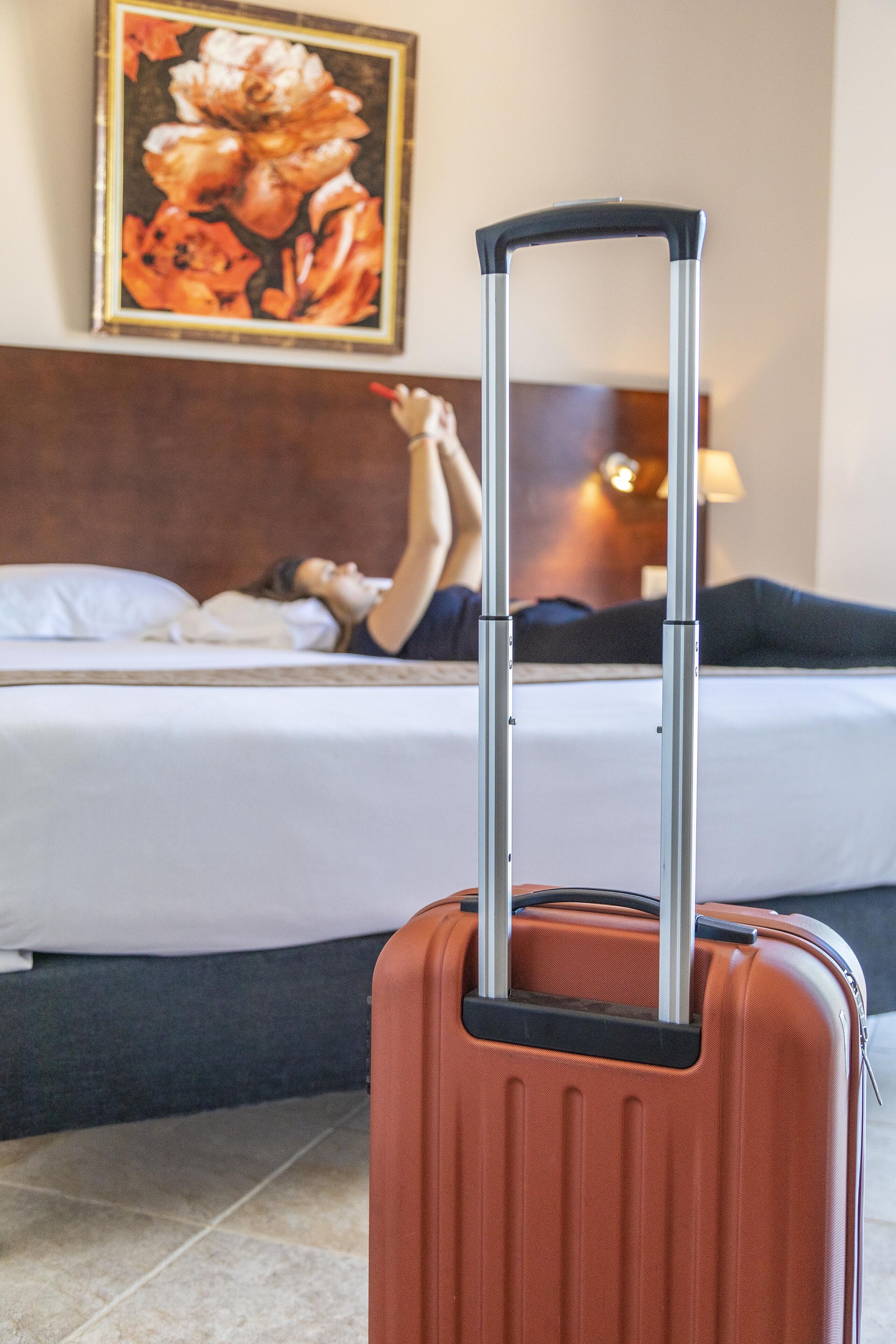A room with a bed, a painting on the wall, and a suitcase in the foreground.