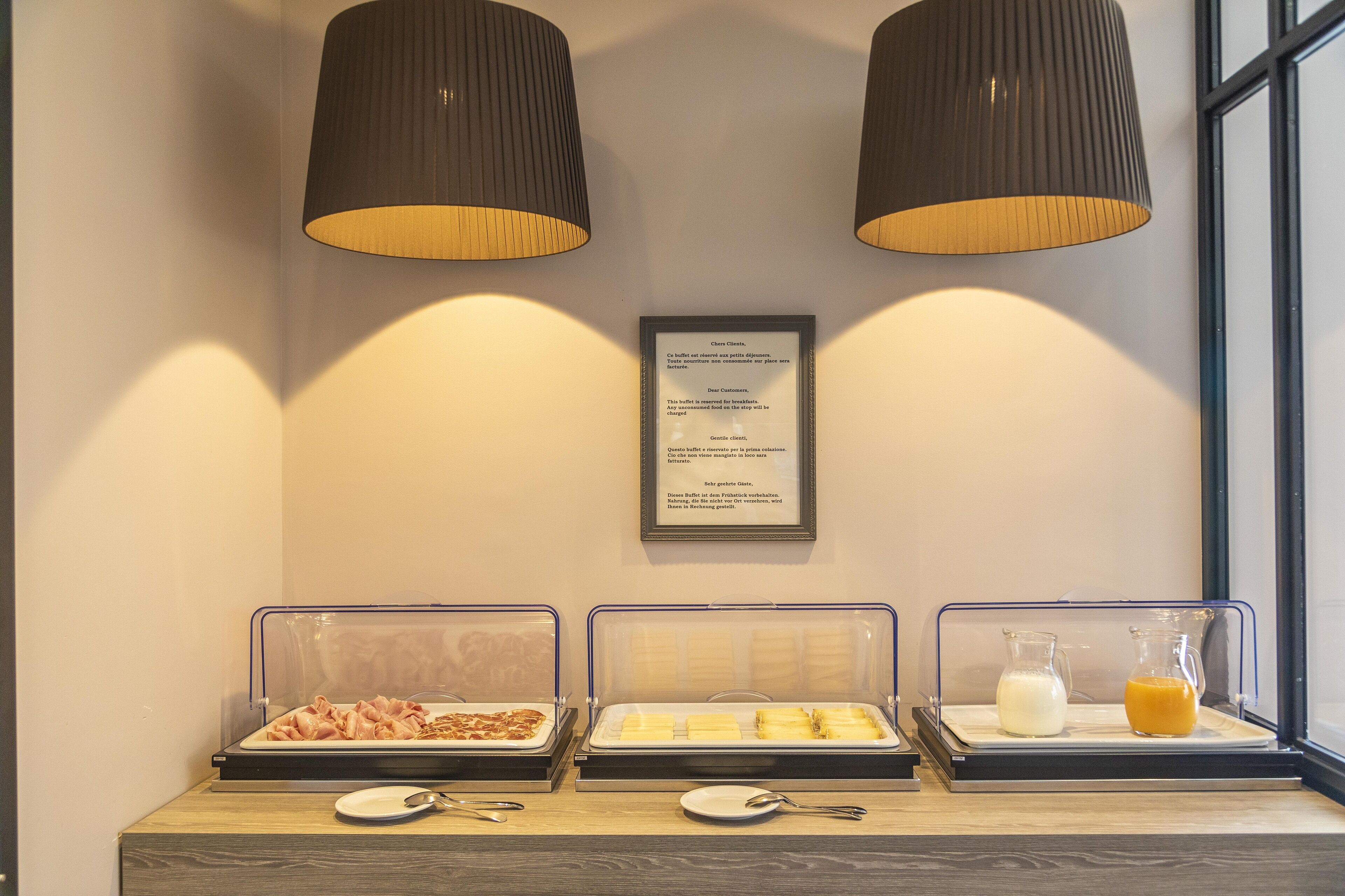 A breakfast buffet with various food items and beverages, a framed menu, and two pendant lights.