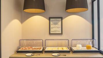 Un buffet della colazione con diversi cibi e bevande, un menu incorniciato e due lampade a sospensione.