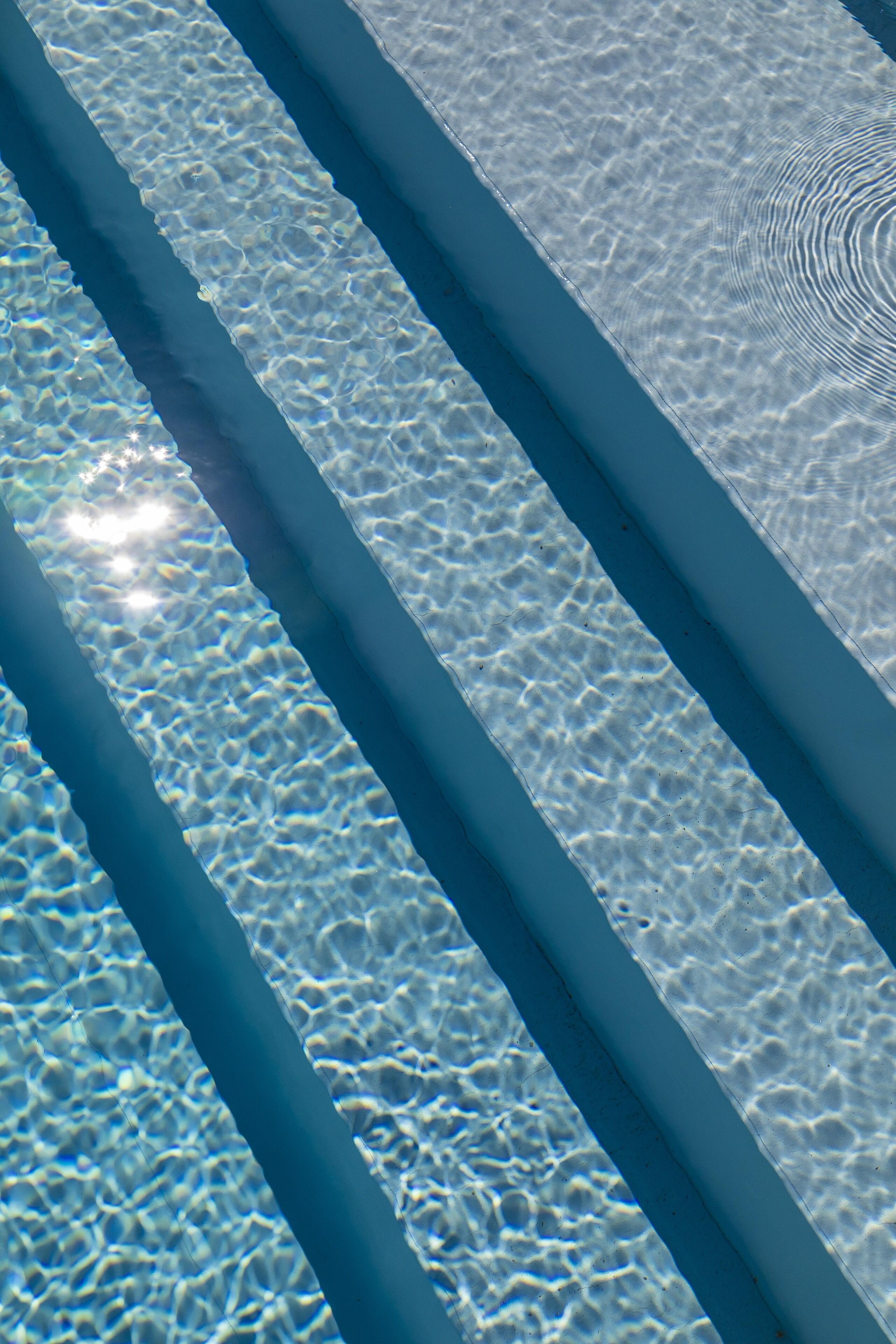 Vista clara de una piscina con líneas paralelas de bordes azules y reflejos de luz en la superficie del agua.