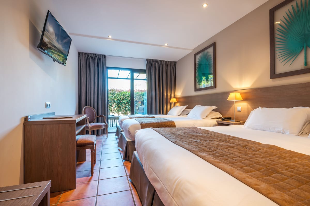 A hotel room with two beds, a desk, a chair, a TV, and a window with curtains.