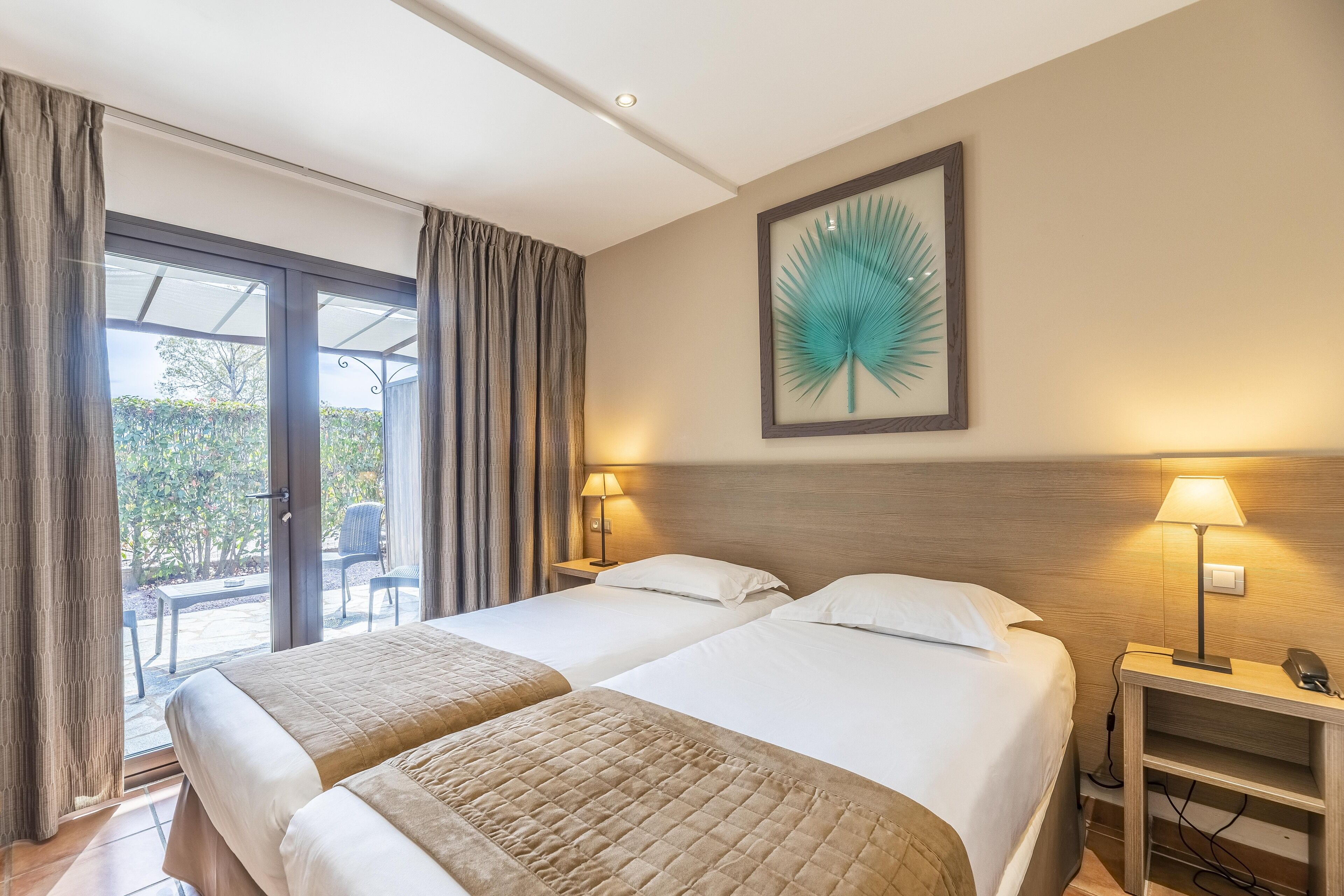 A hotel room with two beds, a large window with curtains, a wall-mounted picture, and bedside lamps.