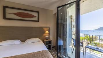 A hotel room with a bed, a nightstand, a framed leaf artwork, and a balcony with a view of the sea.