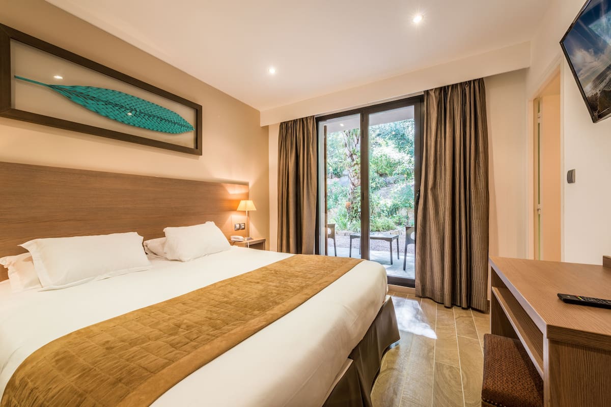 A hotel room with a large bed, a desk, a TV, and a view of the outdoors.