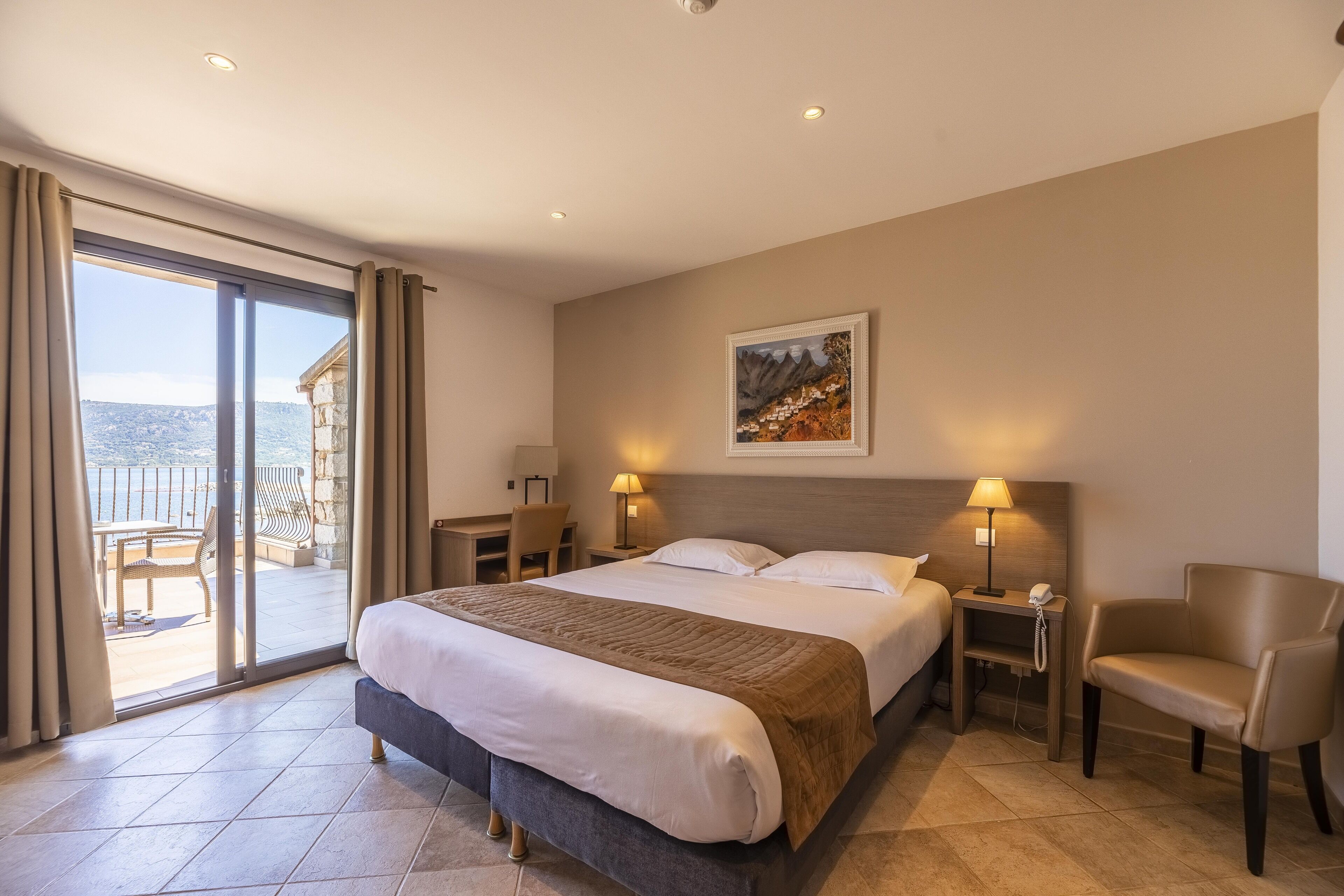 A hotel room with a large bed, a desk, a chair, and a view of the outdoors.