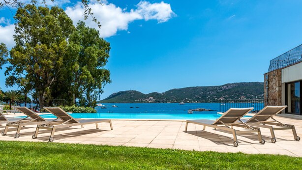 A poolside area with lounge chairs, a clear view of the sea, and a mountainous backdrop. - Hôtel Shegara (Porto-Vecchio)