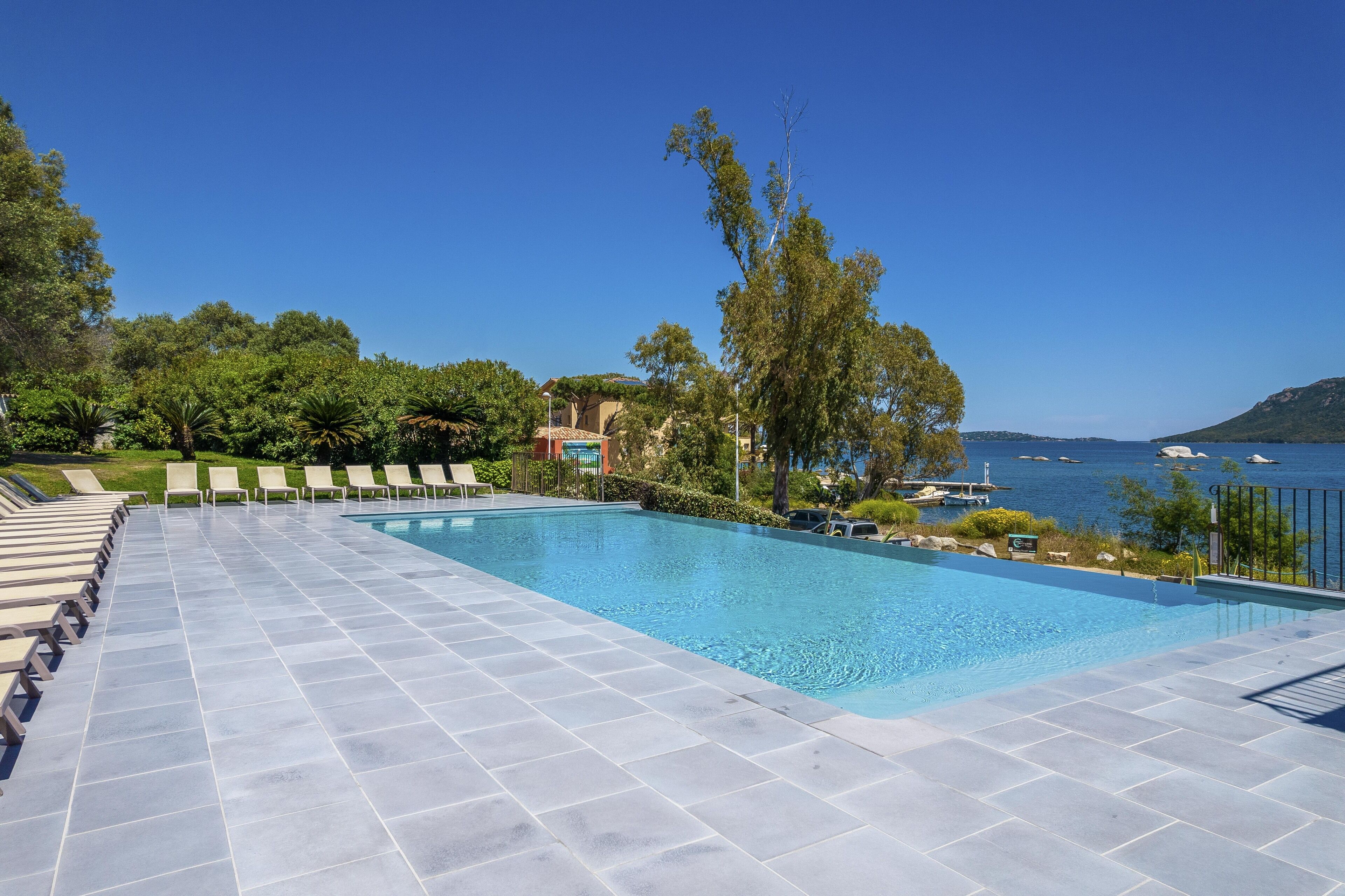 A swimming pool with lounge chairs and a view of the sea.