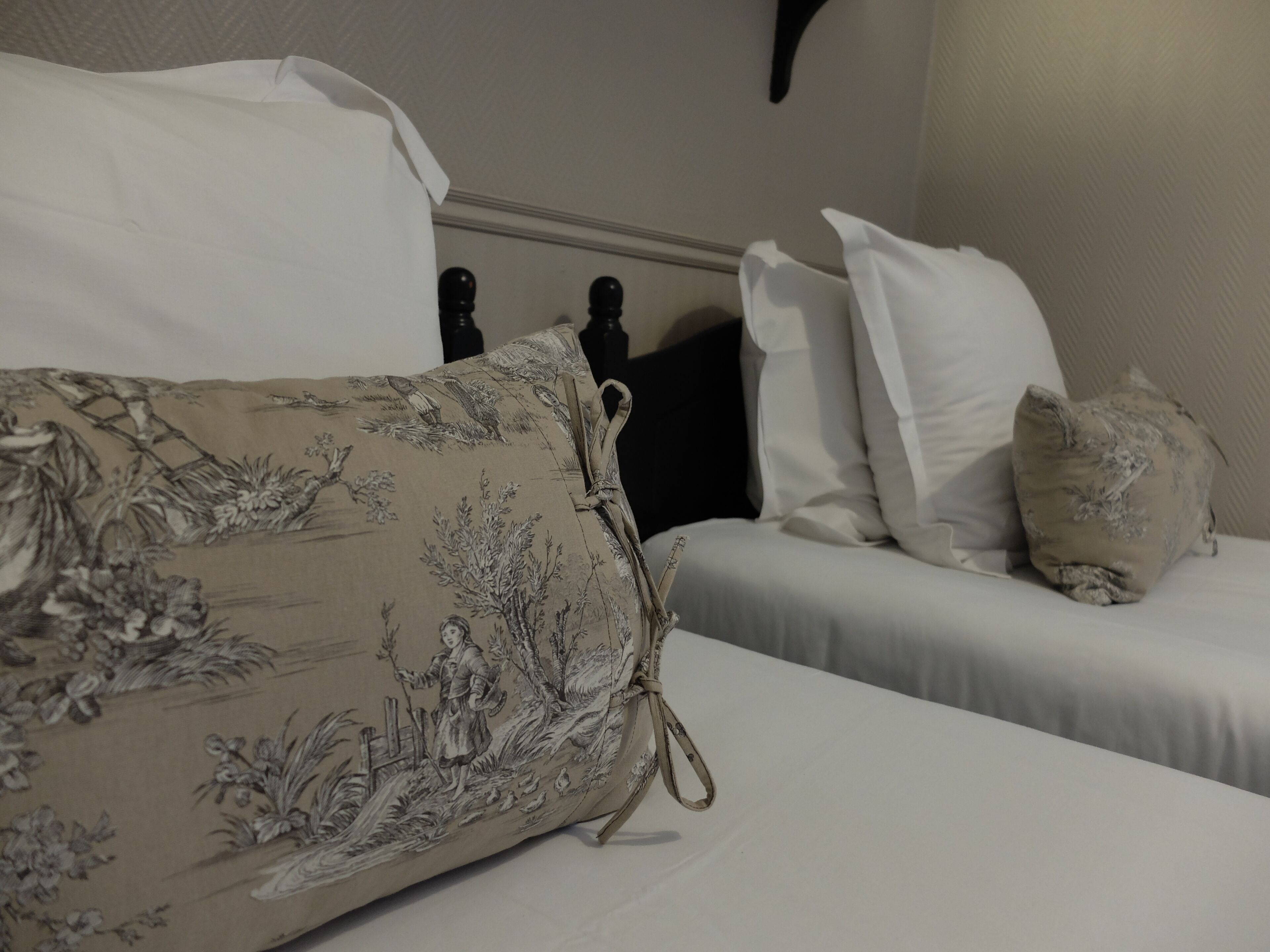 Cama bem arrumada com roupa de cama branca e almofada estampada com flores.