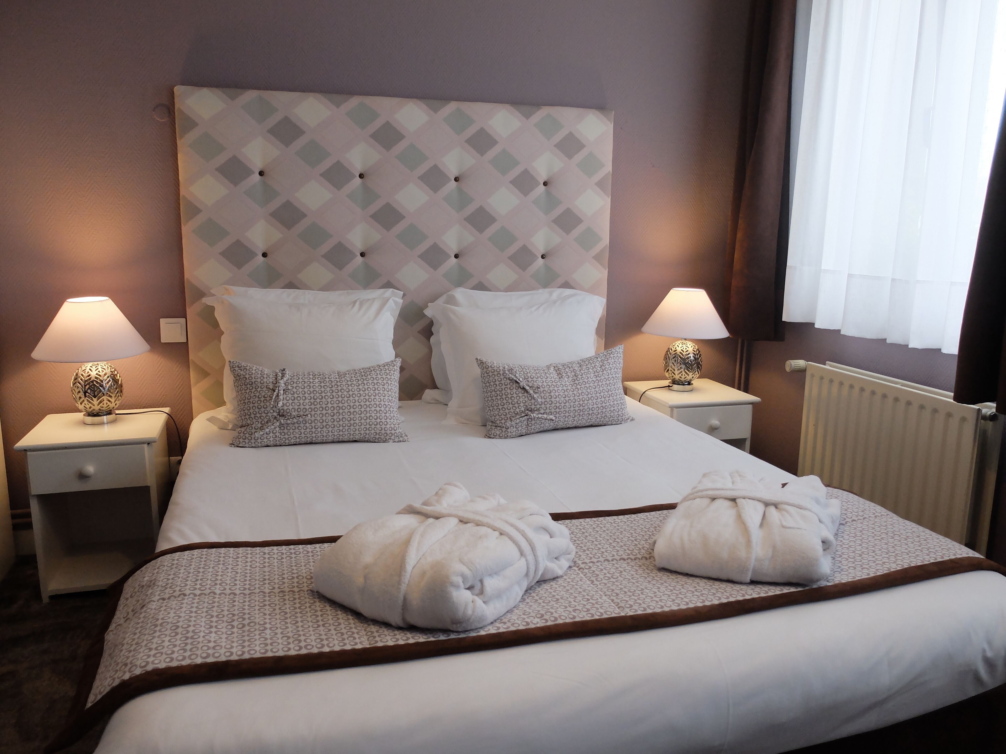 Une chambre d’hôtel avec un grand lit, deux tables de chevet avec des lampes, un radiateur et deux serviettes sur le lit.