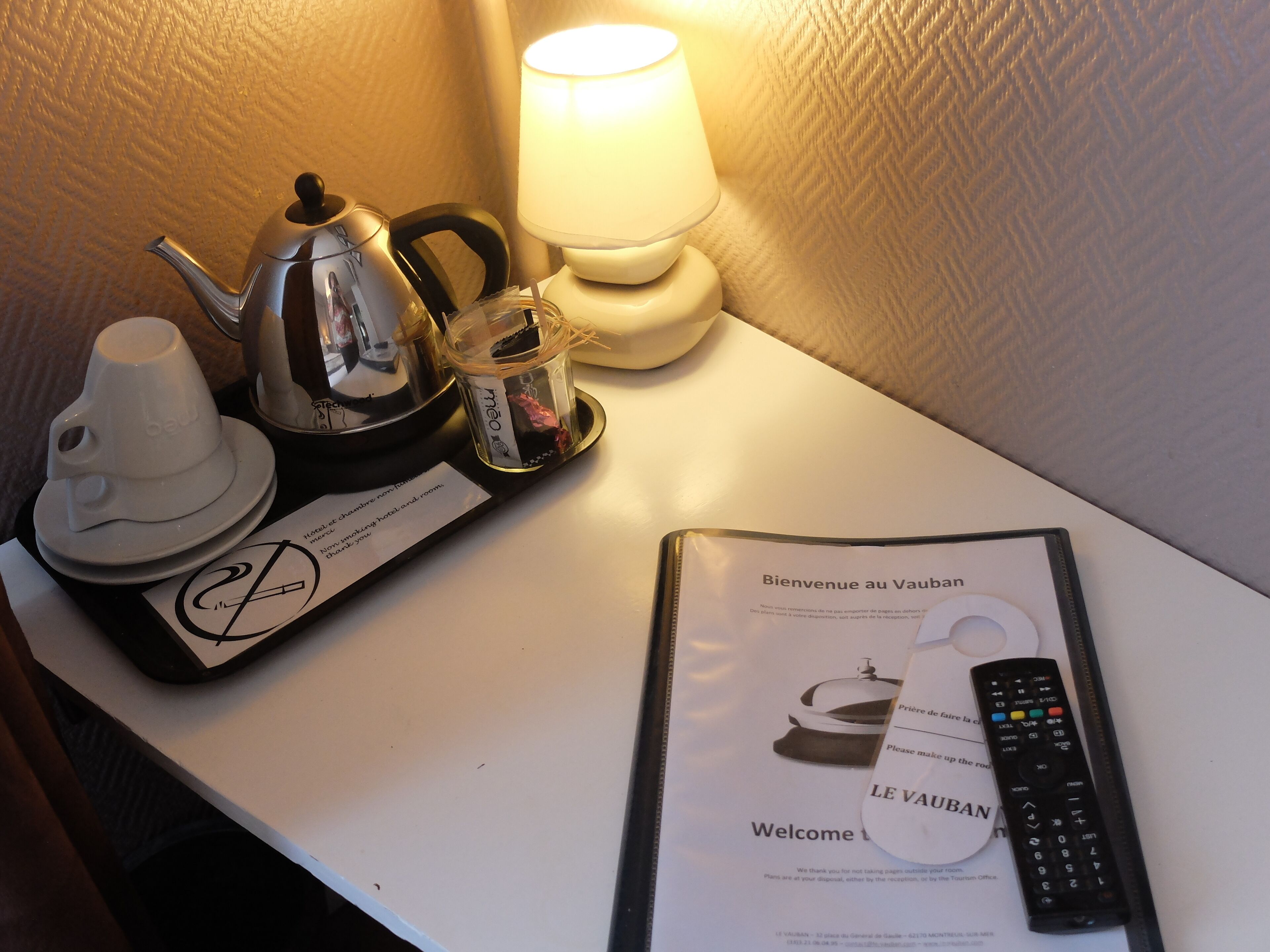 Habitación de hotel con un juego de té, un control remoto y un folleto de bienvenida sobre la mesa.