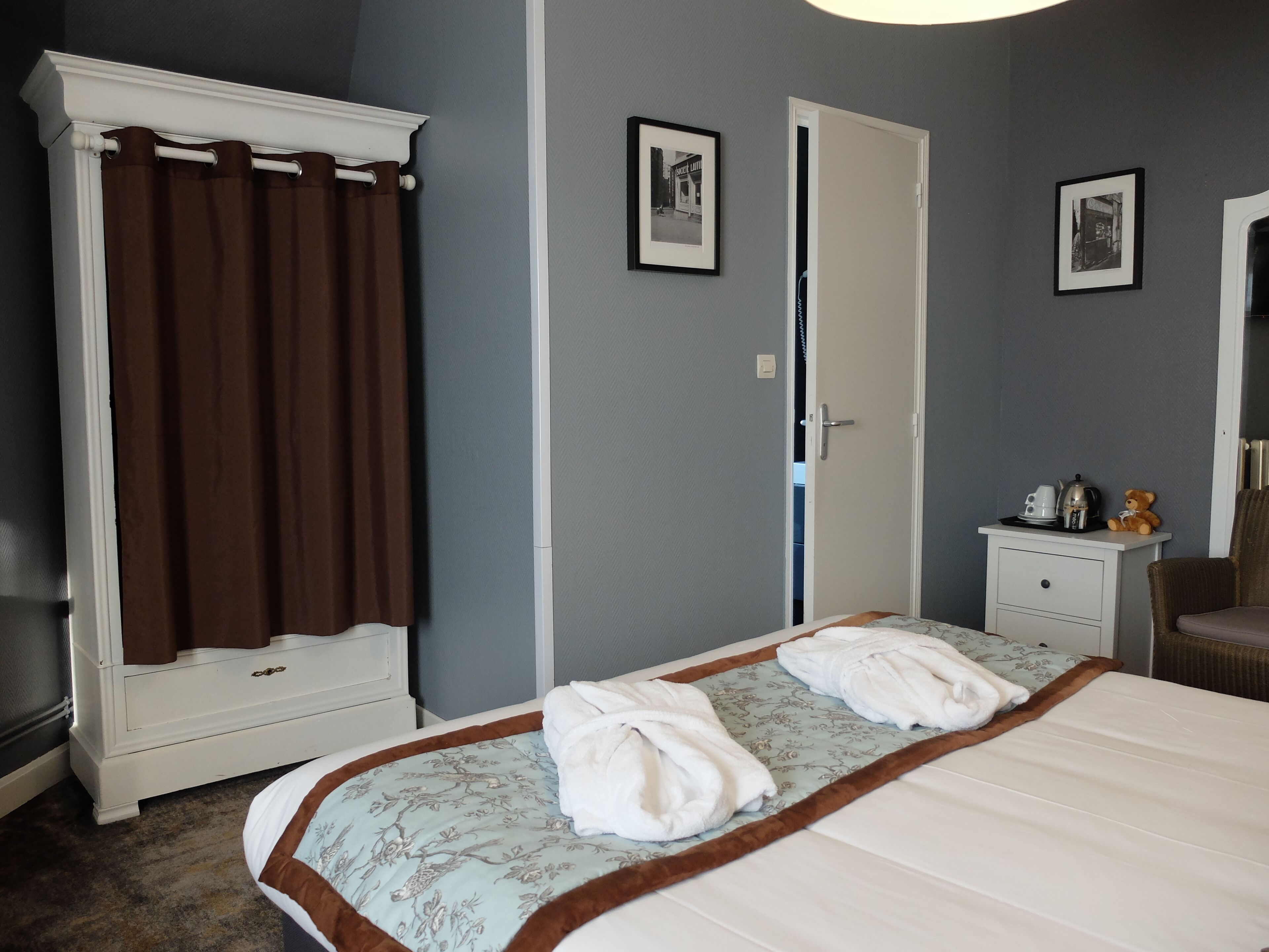 Habitaci ón de hotel con cama, armario, mesita de noche con un osito de peluche y dos cuadros en la pared.
