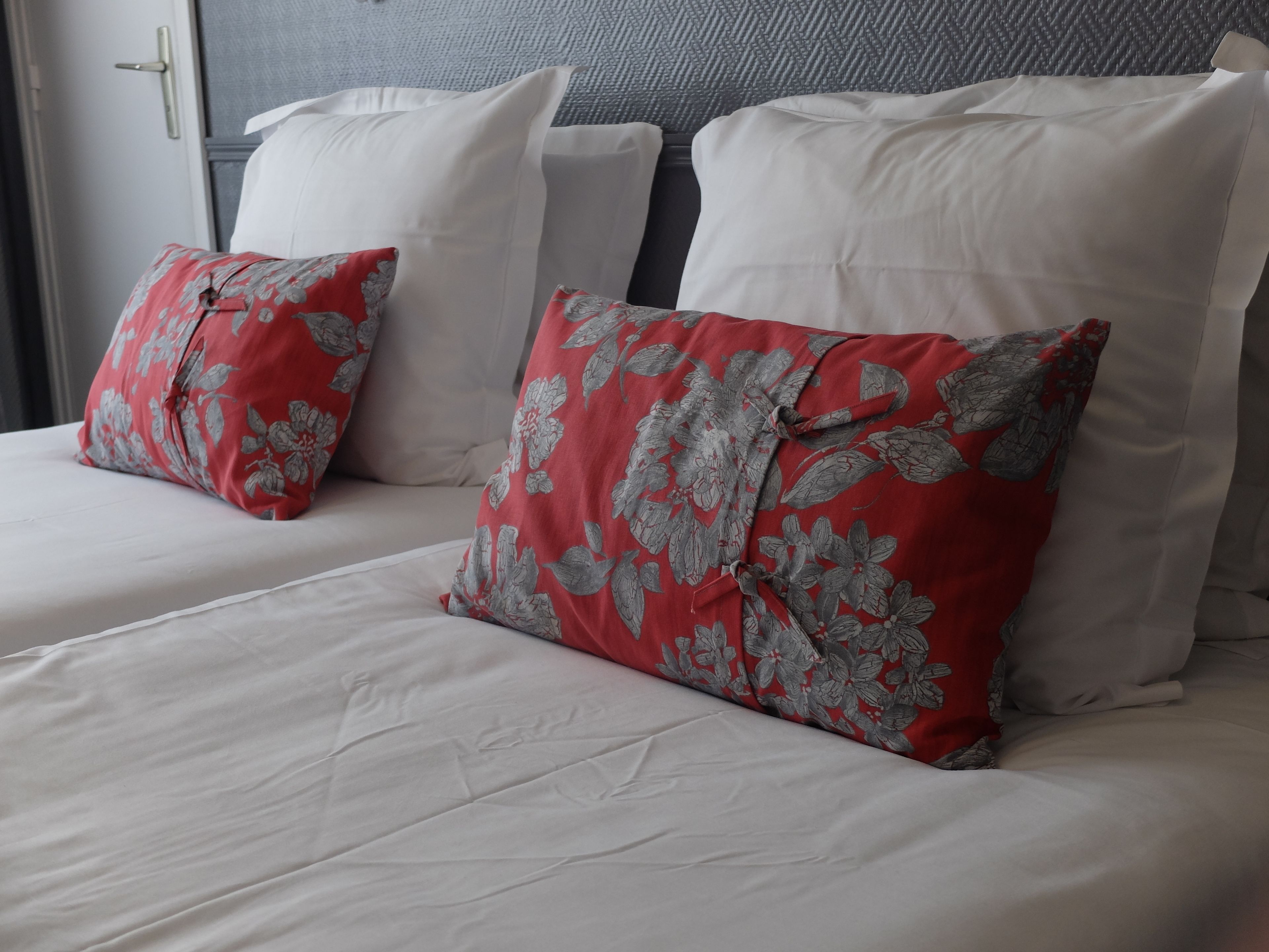 Quarto de hotel com duas camas, cada uma com roupa de cama branca e almofadas estampadas com flores vermelhas.