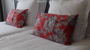 Quarto de hotel com duas camas, cada uma com roupa de cama branca e almofadas estampadas com flores vermelhas.