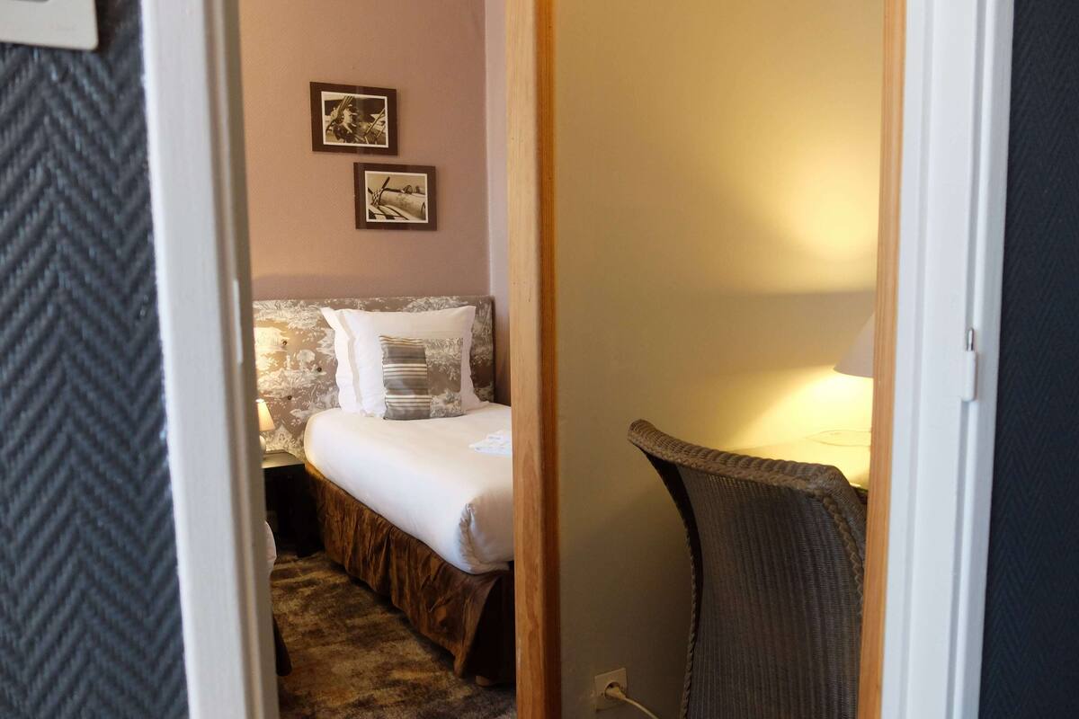 Een knus slaapkamer met een bed, een stoel en twee ingelijste foto’s aan de muur.