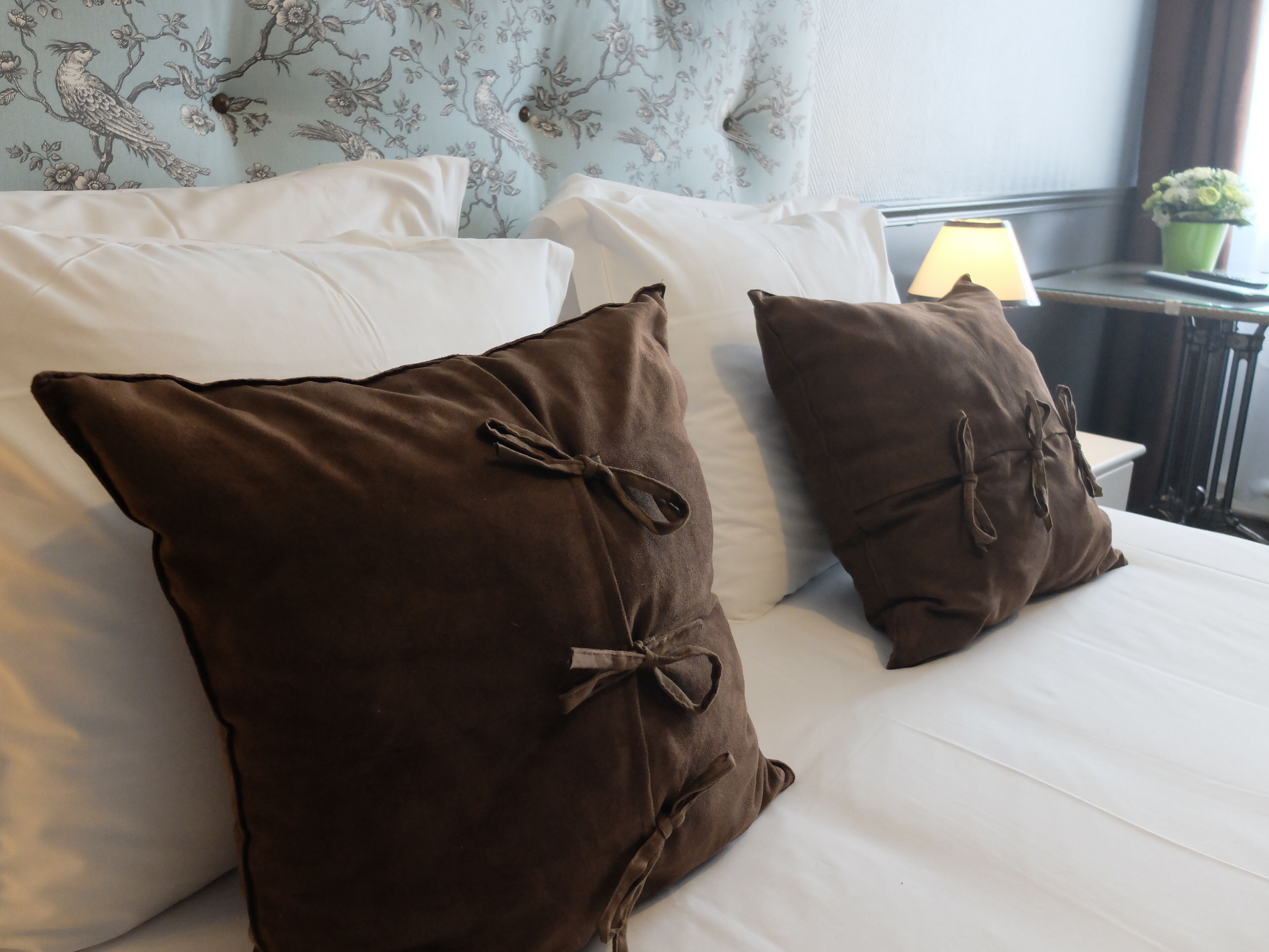 Una cama con sábanas blancas y dos almohadas marrones decoradas con lazos.