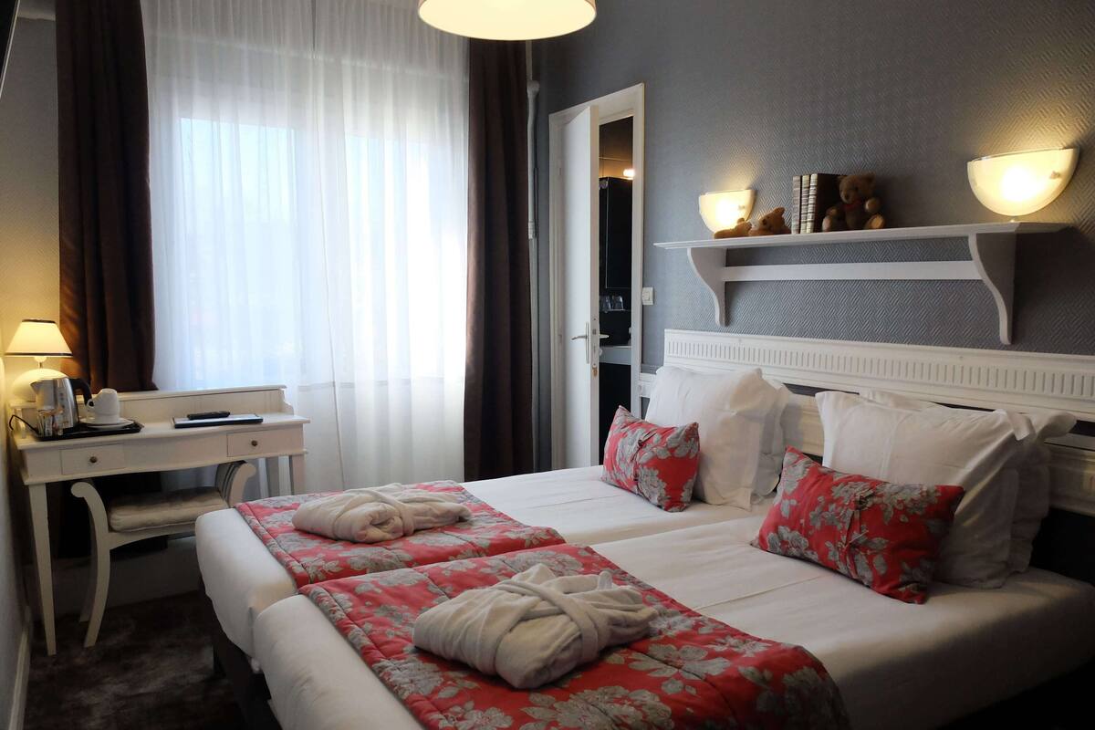 Hotelkamer met twee bedden, een bureau, een stoel, een lamp en een plank met decoratieve objecten.