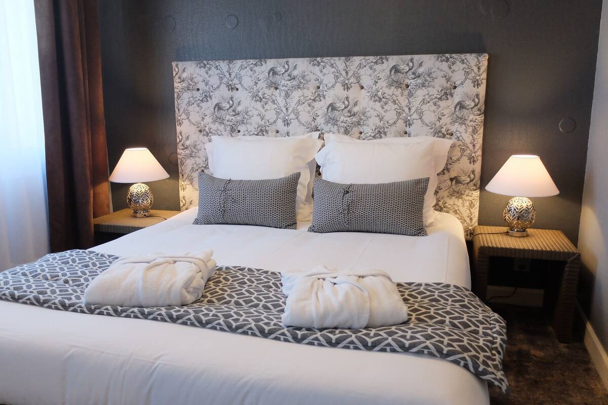 Een net opgemaakt bed met gekleurde kussens en twee nachtlampjes.