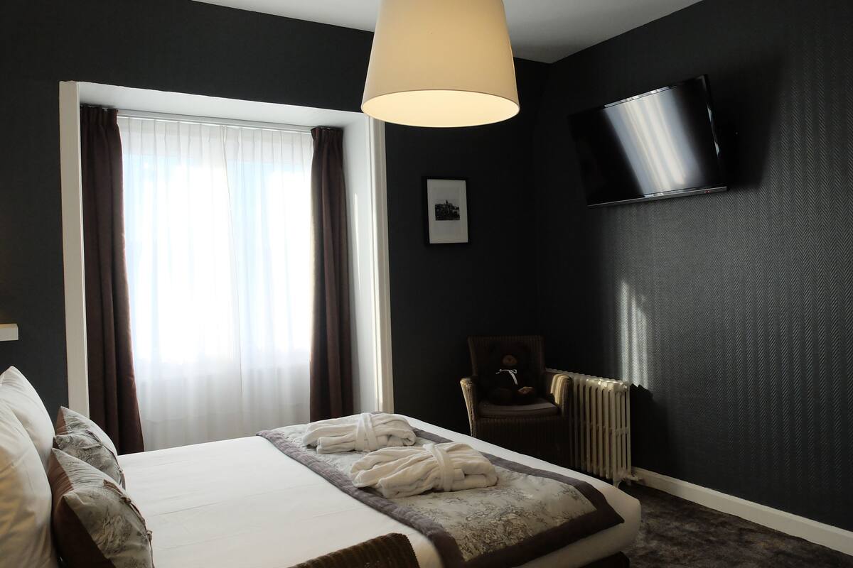 Een hotelkamer met een bed, een stoel, een televisie en een raam met gordijnen.