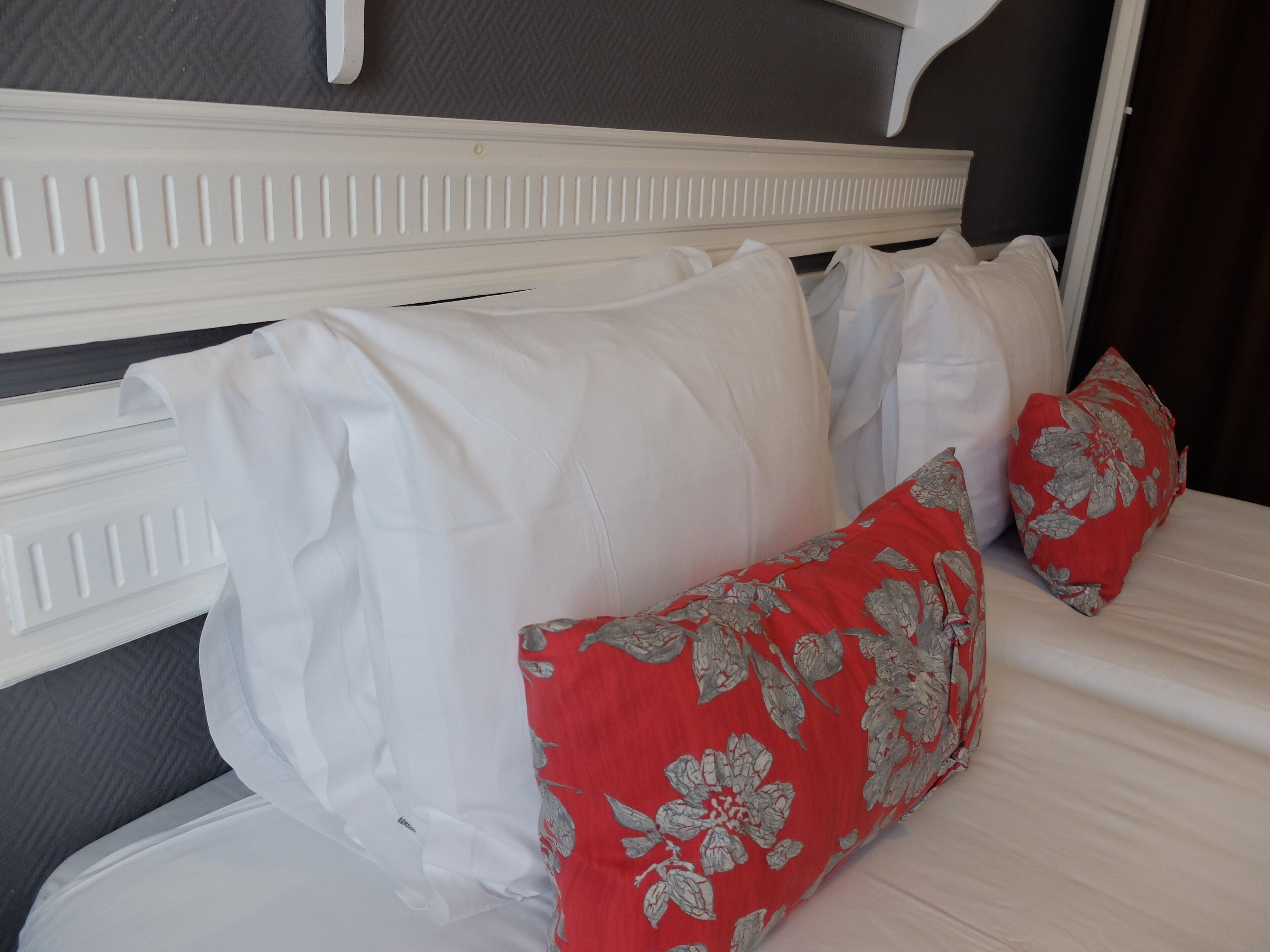 A bed with white bedding and red floral pillows.