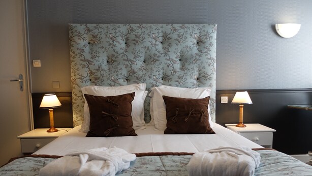 Una cama bien hecha con dos almohadas, dos lámparas de noche y dos toallas sobre la cama.