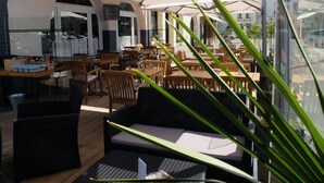 Un café al aire libre con mesas y sillas de madera, un muro de cristal y una pizarra de menú.