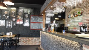 Zona de bar con pared de ladrillo, cuadros enmarcados, una pizarra de menú y una barra con botellas y vasos.